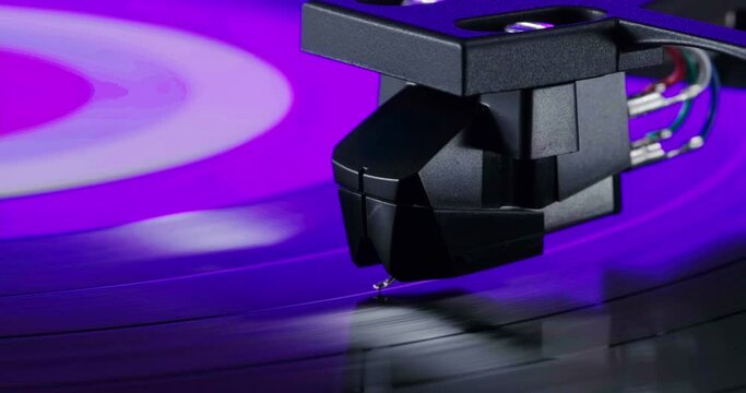 Extreme closeup of tonearm headshell on spinning vinyl record. Party neon flickering light in purple and blue colors flashing on turntable