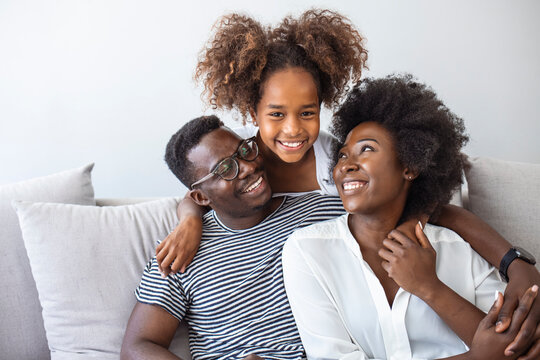 Portrait of happy young african American family with little kid sit relax on couch, smiling black parents rest on sofa hug preschooler children posing for picture at home together