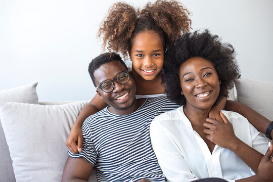 Portrait of happy young african American family with little kid sit relax on couch, smiling black parents rest on sofa hug preschooler children posing for picture at home together