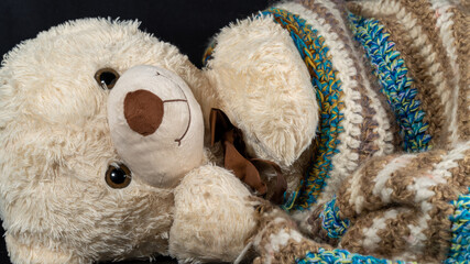 Soft toy white teddy bear wrapped in a knitted blanket, lying to sleep