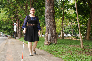 Asian blind person woman walking on sidewalk with a long white cane a mobility tool used to detect...