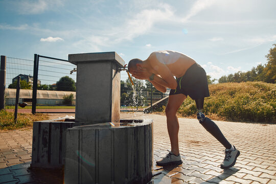 Disabled sportsman refreshes himself at drinking fountain after having sports training outdoors during sunny day.