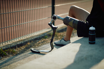 Close-up of disabled sportsman with artificial leg relaxing on staircase outdoors.