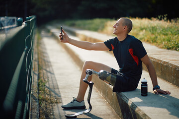 Happy athlete with leg prosthetic has fun while takes selfie with cell phone after practice outdoors.
