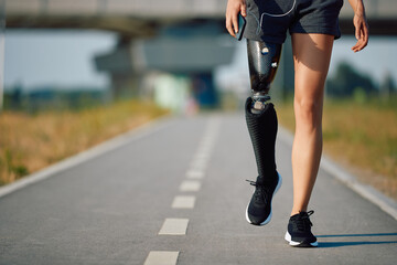 Unrecognizable sportswoman with artificial leg taking a walk along the path outdoors.
