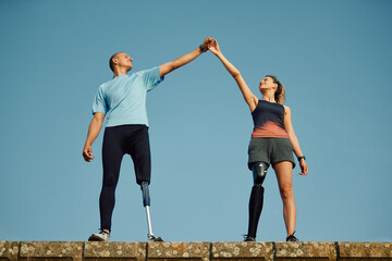 Athletic man and woman with disability supporting each other and holding hands high up against the...