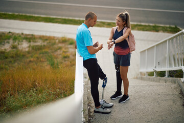 Athletic couple with disability talking outdoors while checking the time on smartwatch.