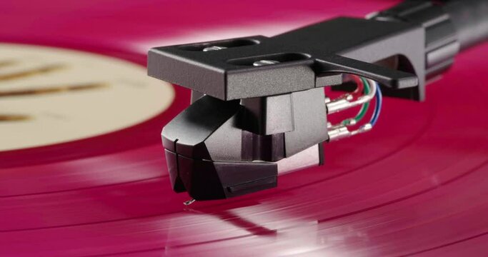 Bright pink vinyl record with beige label spinning on turntable with tonearm headshell on