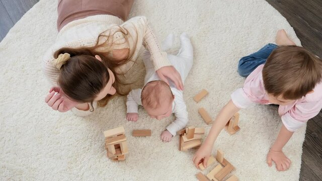 Top view of mother with baby and older son playing on carpet with toy wooden blocks. Parenting, children happiness and family relationship