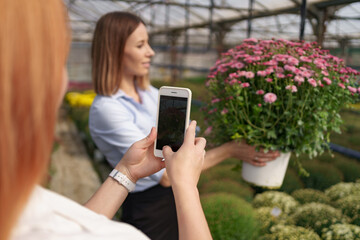 Instagram photographer blogging workshop concept. Close up women's hands holding phone and taking photo of girl with flowers. Selective focus.