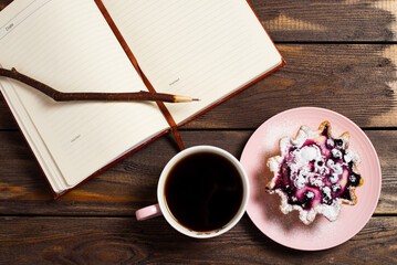 Flatley layout. Open notebook, vintage twig pen, black coffee in a cup and cake basket with berries on an old dark wood table.