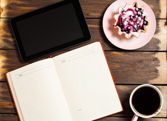 Flatley layout. Open notebook, tablet gadget, black coffee in a cup and a cake basket with berries on a table made of old dark wood.