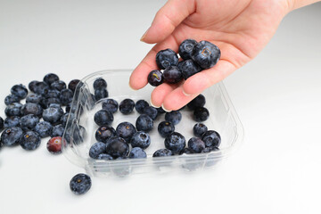 Woman puts blueberries in plastic box. Healthy eating, dieting, vegetarian food and people concept - close up of woman hands holding blueberries. 
