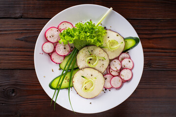 A salad of thinly sliced radish, cucumber, radish with green onions is beautifully laid out on a flat plate, sprinkled with a mixture of peppers and coarse salt and poured with olive oil. The plate is