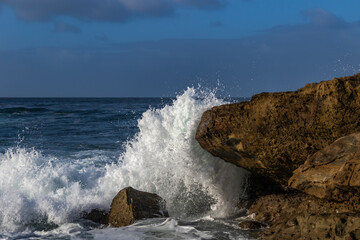 Wave breaking on rock in Laguna Beach, California. Pacific ocean, blue sky and clouds in background.
