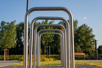 Metalowe stojaki rowerowe w parku, zielone drzewa w tle