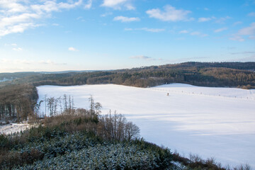Fototapeta na wymiar View of a winter snowy landscape with a small hill, forest and blue sky