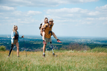 Group of young friends having fun while hiking in nature. Man with leg disability is carrying his...