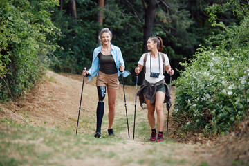 Happy woman with leg prosthesis hikes through the wood with her female friend.