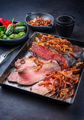 Traditional Commonwealth Sunday roast with sliced cold cuts roast beef with fried onion rings and chili served as close-up on an old rustic metal tray