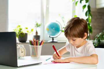 The little boy doing lessons at home at the table in front of the laptop, distance learning online education.