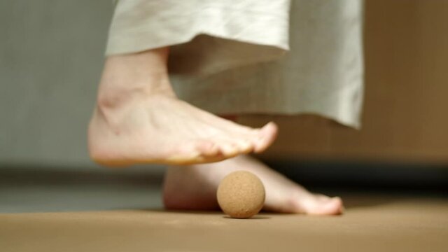 Close up video of woman dressed in natural linen jumpsuit placing cork ball on cork mat for myofascial release practices. Concept: self care practices at home