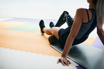 Athletic woman with prosthetic leg prepares for working out and uses foam roller at gym.