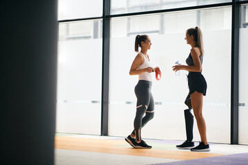 Fototapeta premium Happy female athletes talking while taking a break from exercising at gym. One of them has prosthetic leg.