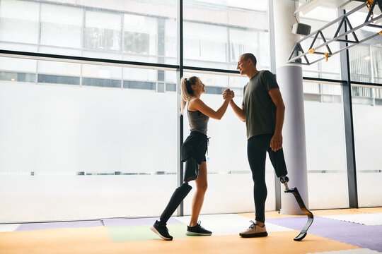 Happy athletic man and woman with leg disability greeting each other during sports training at gym.
