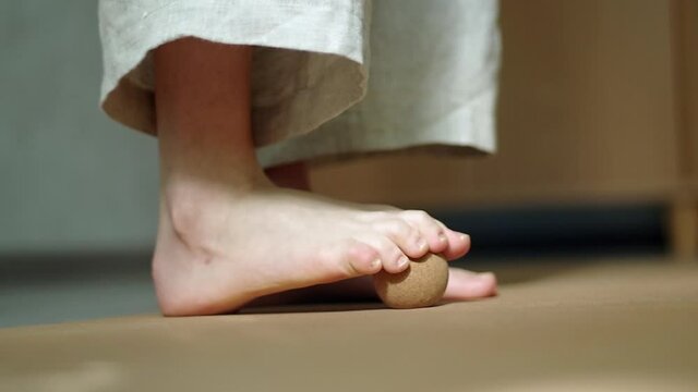 Woman wearing linen walking in on a cork mat, doing myofascial release MFR practices on a cork ball. Concept: self care practices at home