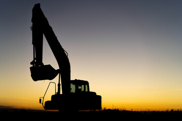black silhouette of an excavator on the background of the sunset sky, place for text