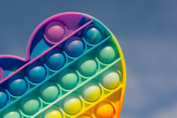 colorful antistress sensory toy fidget push pop it on sky background. rainbow pop it heart - obrazy, fototapety, plakaty