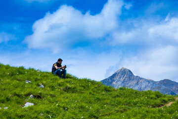 Fototapeta na wymiar man sitting on the top of the flowered mountain and looks at the phone