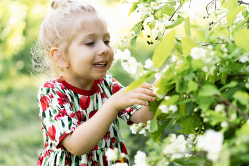 Happy little girl in summer in flowers, portrait of a blonde girl in nature