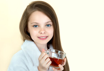 Cute little girl is drinking tea. Kid holds hot beverage