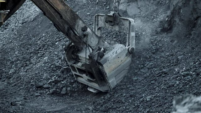Close-up of an excavator bucket picking up ore in an open pit.