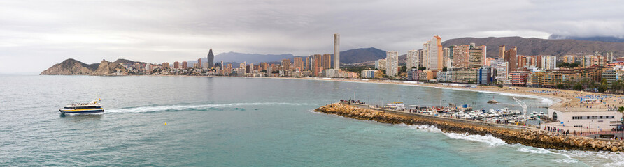 Fototapeta premium Panoramic view of the Poniente beach in Benidorm with its skyscrapers facing the sea from the Balcon del Mediterraneo and tourist boat 