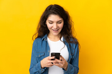 Teenager Russian girl isolated on yellow background sending a message or email with the mobile