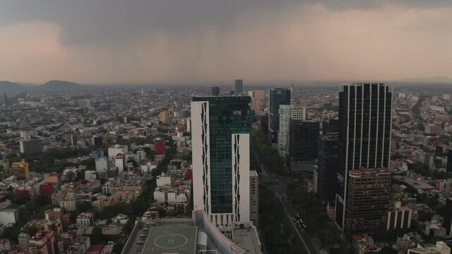 Aerial drone view of tall modern office buildings along wide boulevard. Camera view trucking to right. Dramatic cloudy sky before heavy rain or storm. Mexico city, Mexico.