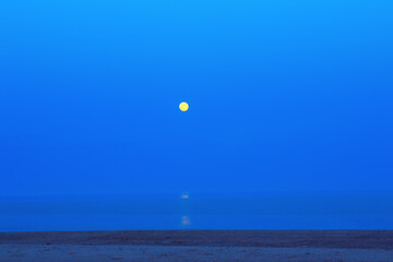 Full moon over the sea with reflection in the water . Calm sea in the daybreak