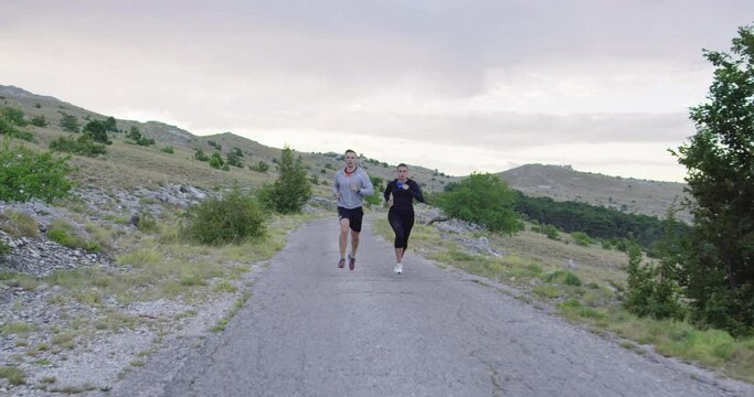 Tracking slow motion shot of sportive couple jogging outdoors in the morning, trail running experience in nature. Healthy lifestyle concept.