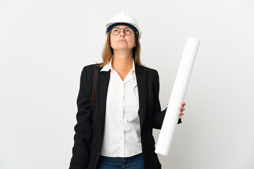 Middle age architect woman with helmet and holding blueprints over isolated background and looking up