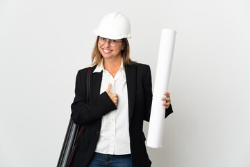 Middle age architect woman with helmet and holding blueprints over isolated background giving a thumbs up gesture