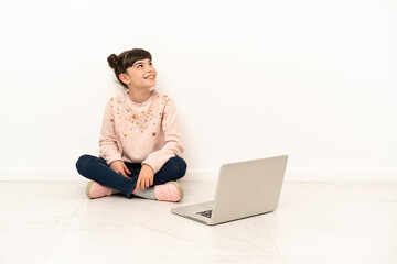 Little girl with a laptop sitting on the floor thinking an idea while looking up