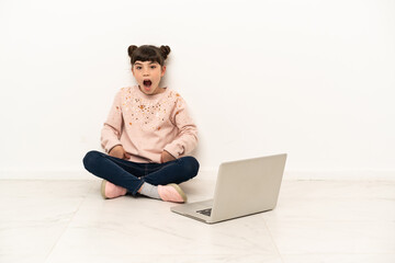 Little girl with a laptop sitting on the floor with surprise facial expression