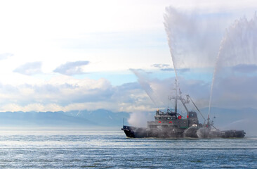Naklejka na ściany i meble Floating tug boat is spraying jets of water