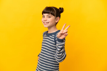 Little caucasian girl isolated on yellow background smiling and showing victory sign