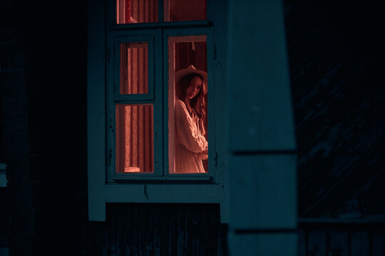 photo from the street to the mysterious girl who stands in the window, in a room with the lights on. Creative photography. High quality photo