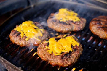 Hamburgers with cheddar cheese grilling on a gas barbecue.