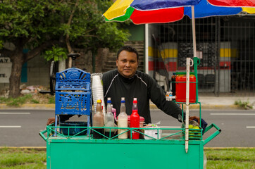 Hispanic person street seller in a colorful food cart smiling 